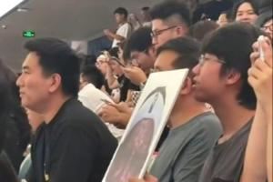 詹姆斯中國行成都活動現場 一球迷拿著詹姆斯經典哭臉照坐在場邊